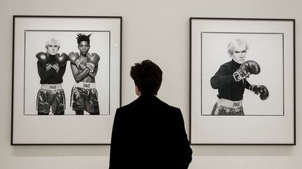 Un visiteur de l'exposition "Basquiat x Warhol à quatre mains" à la Fondation Vuitton, devant deux photos de Michael Halsband prises en 1985 pour annoncer leur première exposition commune à la Tony Shafrazi Gallery de New York, débutée en septembre 1985. (BERTRAND GUAY / AFP)