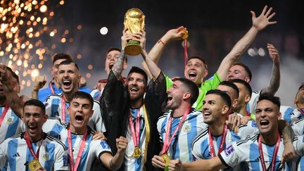 Entouré de ses coéquipiers, Lionel Messi, capitaine de l'équipe d'Argentine et vêtu d'un bisht, porte la Coupe du monde après la victoire contre l'équipe de France de football, le 18 décembre 2022. (FRANCK FIFE / AFP)