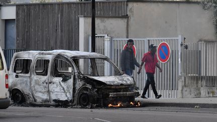 Des habitants des Grésilles passent à côté d'un véhicule calciné, le 15 juin 2020, à Dijon (Côte-d'Or). (PHILIPPE DESMAZES / AFP)