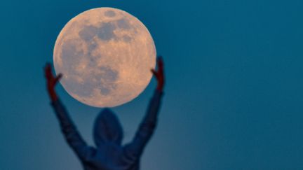 Un homme fait mine de tenir la Lune, le 7 avril 2020, à&nbsp;Sieversdorf&nbsp;(Allemagne). (PATRICK PLEUL / DPA-ZENTRALBILD / AFP)