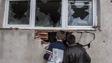 Deux gar&ccedil;ons regardent &agrave; travers un trou dans le mur d'une maison caus&eacute; par des combats, &agrave; Kumanovo,&nbsp;en Mac&eacute;doine, le 11 mai 2015. (ARMEND NIMANI / AFP)