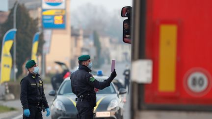 Des membres de la police douanière et financière italienne, portant des masques de protection contre le nouveau coronavirus, contrôlent un véhicule à&nbsp;Casalpusterlengo (Italie), le 24 février 2020.&nbsp; (YARA NARDI / REUTERS)