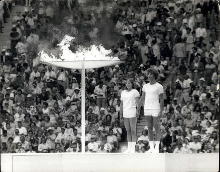 Deux jeunes athlètes canadiens se tiennent devant la flamme olympique avant le début des JO&nbsp;de Montréal, le 20 juillet 1976. (KEYSTONE PICTURES USA / KEYSTONE / MAXPPP)