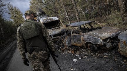 Un soldat ukrainien marche à côté de voitures calcinées, le 5 octobre 2022, à Lyman (Ukraine),ville reprise aux troupes russes lors de la contre-offensive. (METIN AKTAS / ANADOLU AGENCY / AFP)