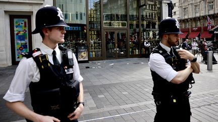 Deux policiers britanniques à proximité du lieu de l'attaque au couteau survenue à Londres, lundi 12 août 2024. (BENJAMIN CREMEL / AFP)