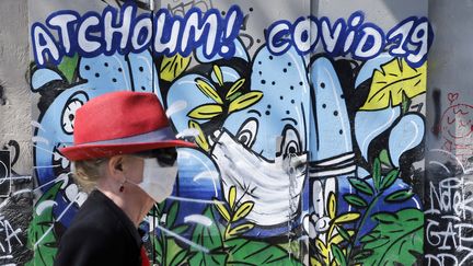 Une femme marche devant une fresque murale où est écrit "Atchoum ! Covid-19" dans les rues de Paris, le 20 avril 2020. (CHESNOT / GETTY IMAGES EUROPE)