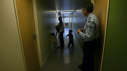 Un policier regarde une jeune femme et ses deux enfants, le 27 octobre 2003, dans un couloir du centre de rétention de la zone d'attente de l'aéroport de Roissy-Charles de Gaulle (JOEL ROBINE / AFP)