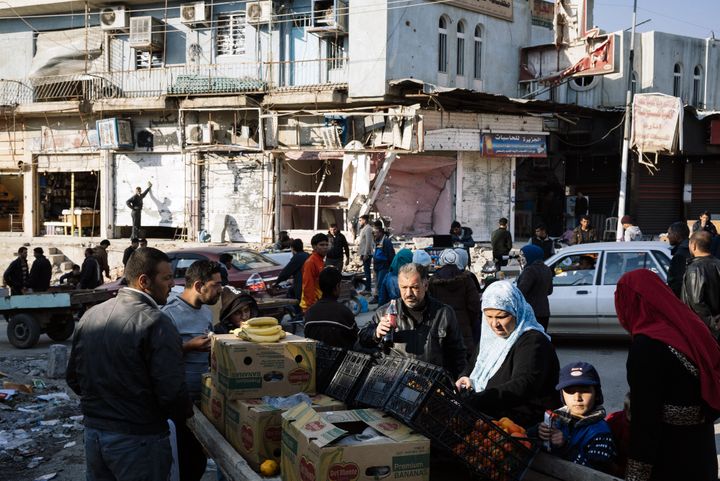 Une famille irakienne achète des fruits sur un étal du marché  d'Al-Zahraa, mercredi 18 janvier 2017 à Mossoul (Irak). Les combats ont entraîné des dégâts importants sur les bâtiments. (DIMITAR DILKOFF / AFP)