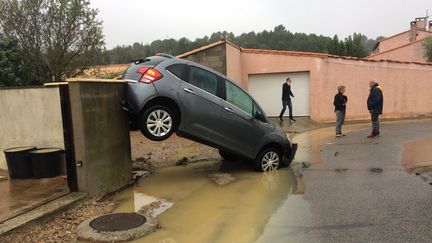 Des habitants de&nbsp;Villegailhenc (Aude) près d'une voiture emportée par les flots, le 15 octobre 2018. (ERIC CABANIS / AFP)