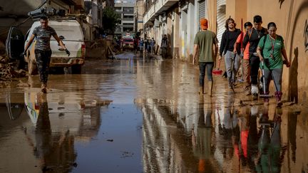 Des personnes dans une rues couvertes de boue, à Alfafar, dans la région de Valence, en Espagne, le 5 novembre 2024. (ALBERT LLOP / NURPHOTO / AFP)