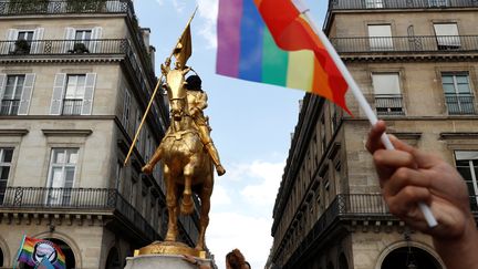 Des manifestants agitent des drapeaux arc-en-ciel, le 30 juin 2018, lors de la Marche des fiertés, à Paris, devant la statue de Jeanne d'Arc couverte d'un tissu noir. (GEOFFROY VAN DER HASSELT / AFP)