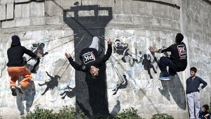 De jeunes Palestiniens s'exercent au parkour sur un mur habill&eacute; par une oeuvre du street artiste Banksy &agrave; Beit Hanoun (Palestine), le 13 mars 2015. (MOHAMMED ABED / AFP)