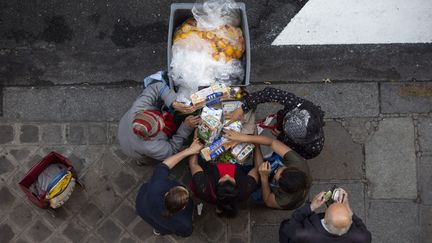 Des personnes récupérant des aliments consommables dans une poubelle devant un supermarché, à Paris. (MATTHIEU DE MARTIGNAC / MAXPPP)