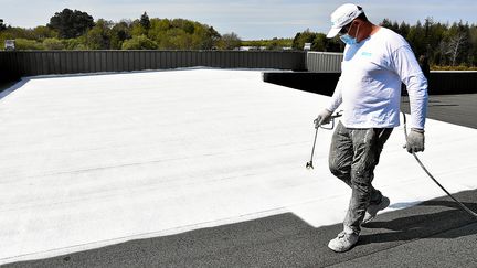 Un homme peint en blanc un toit. Une peinture réflective à base de coquilles d'huîtres mise au point par Cool Roof France, à Brandérion (Morbihan). (MAXPPP)