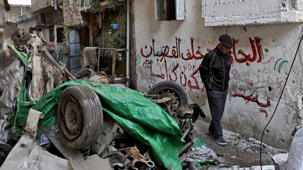 Un homme passe à côté d'une voiture détruite par un bombardement israélien, le 9 janvier 2024, en Cisjordanie occupée. (ZAIN JAAFAR / AFP)