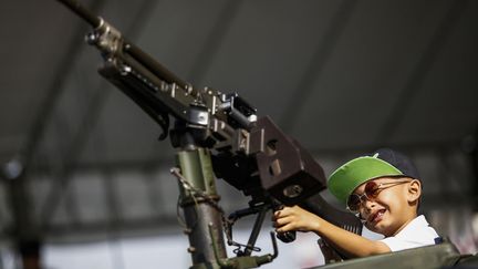 Un jeune gar&ccedil;on s'amuse avec un fusil mitrailleur non charg&eacute; lors d'une journe&eacute;e porte-ouvertes dans une base militaire &agrave; Bangkok (Tha&iuml;lande), le 11 janvier 2014. (ATHIT PERAWONGMETHA / REUTERS)