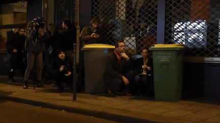 Des personnes, dont des journalistes, se protègent derrière des poubelles à proximité du Bataclan, à Paris. (DOMINIQUE FAGET / AFP)