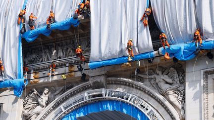 Les cordistes, en rappel, déploient le tissu en polypropylène fabriqué spécialement en Allemagne. Il est bleu côté pile et argenté côté face,. Un kilo d'aluminium a été puvérisé sur les 25 000 m2 d'étoffe qui emballent le monument. (THOMAS SAMSON / AFP)