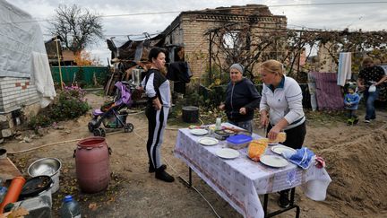 Une famille s'apprête à diner à côté d'une maison détruite dans le village de Gorenka, dans la région de Kiev. (SERGEI CHUZAVKOV / AFP)