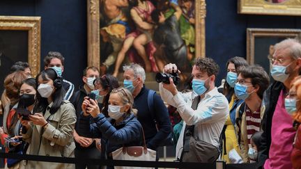 Des visiteurs masqués prenant des photots de la Joconde de Léonard de Vinci au musée du Louvre à Paris. (ALAIN JOCARD / AFP)