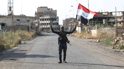 Un policier irakien brandit le drapeau de son pays, le 9 juillet 2017 dans la vieille ville de Mossoul, libérée de l'Etat islamique. (AHMAD AL-RUBAYE / AFP)