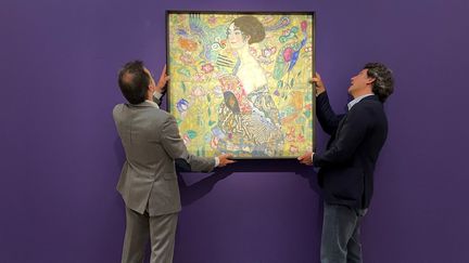 Des employés posent avec l'œuvre la "Dame à l'éventail" de l'artiste autrichien Gustav Klimt, le 20 juin 2023, à la maison de vente aux enchères de Sotheby's, dans le centre de Londres. (MATHILDE BELLENGER / AFP)