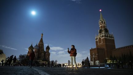 Une femme utilise son smartphone sur la place rouge à Moscou (Russie), tandis que la tour Spasskaya du Kremlin et la Cathédrale Basile-le-Bienheureux sont éteintes pour l'Eeath Hour, le 27 mars 2021. (PAVEL GOLOVKIN / AP)