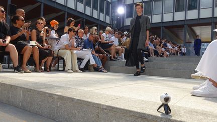 Si le placement au 1er rang (first row dans le jargon mode) est royal, être installé au deuxième rang peut rendre difficile la prise de photo. Un journaliste a trouvé la solution en positionnant son appareil au ras des marches version first row !
 (Corinne Jeammet)