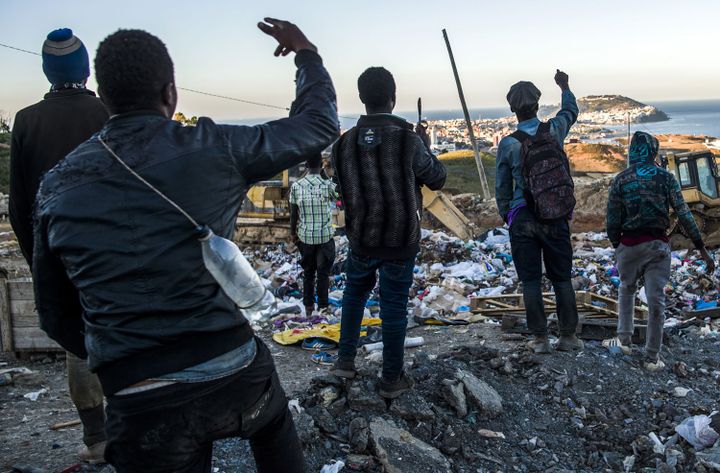 Les jeunes migrants africains saluent en regardant l'enclave espagnole de Ceuta depuis la décharge de Fnideq, le 5 juillet 2018. Dressée à l'horizon, elle est la dernière étape sur le continent africain pour des milliers de migrants qui passent des mois ou des années à tenter de rejoindre l'Europe.  ( FADEL SENNA/AFP)