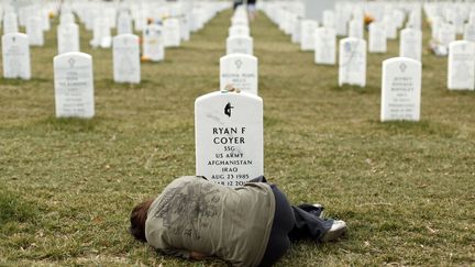 Une jeune femme est allong&eacute;e devant la tombe de son fr&egrave;re, mort apr&egrave;s avoir &eacute;t&eacute; bless&eacute; en Afghanistan, cimeti&egrave;re d'Arlington (Virginie, Etats-Unis), le 11 mars 2013. (KEVIN LAMARQUE / REUTERS)