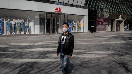 Un passant devant la boutique H&amp;M de Pékin (Chine), le 19 mars 2020. (NICOLAS ASFOURI / AFP)