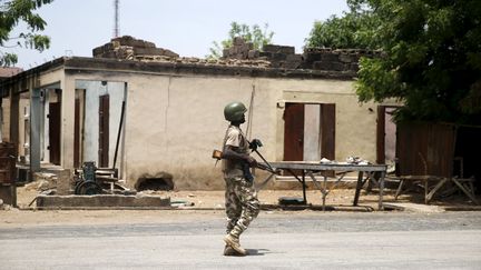 Un soldat nigérian passe devant un bâtiment incendié à Michika, au Nigeria, que l'armée vient de reprendre à Boko Haram, le 10 mai 2015. (AKINTUNDE AKINLEYE / REUTERS)