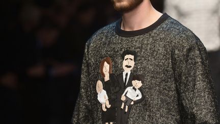 Chez Dolce &amp; Gabbana, le mot d'ordre est "Familles, je vous adule". Tels des statues dans un musée de cire, ils sont tous debout là en un portrait géant et vivant, des aïeux, des moyens, des jeunes et même un bébé, en tout 5 familles habillées de sombre, illustrant et assistant au défilé en même temps. On les retrouve en photo ou en dessin sur les sweaters de la collection intitulée "DG Family". D'autres arborent des motifs de tableaux classiques ou proclament des slogans comme "L'amour pour toujours", "Sicile" ou "Je t'aime tant".
 (TIZIANA FABI / AFP)