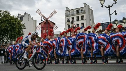 Moulin rouge. Valentin Madouas, futur médaille d'argent de la course en ligne, passe devant les filles du célèbre cabaret, lors du passage dans un Paris noir de monde pour assister à cette course, le 3 août 2024. (MAURO PIMENTEL / AFP)