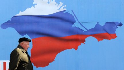 Un homme passe devant une affiche repr&eacute;sentant le territoire de la Crim&eacute;e aux couleurs de la Russie, &agrave; S&eacute;bastopol (Ukraine), le 11 mars 2014. (VIKTOR DRACHEV / AFP)