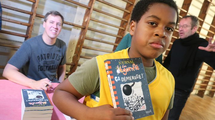 Roy, 11 ans, en 6e au collège Georges Rouault pose avec "Le journal d'un dégonflé" (Seuil Jeunesse) et l'auteur Jeff Kinney (en arrière plan), le 10 décembre 2019 (Laurence Houot / franceinfo Culture)