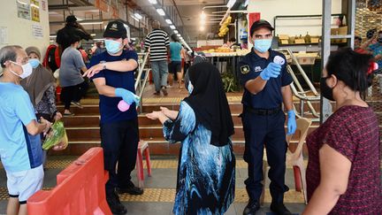 Des agents de sécurité désinfectent les mains des visiteurs d'un marché et vérifient leur température, le 29 mai 2020 à Penang, en Malaisie. (GOH CHAI HIN / AFP)