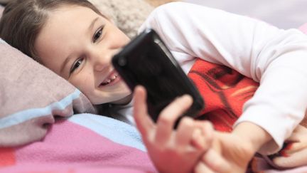 Une petite fille consulte un téléphone portable dans sa chambre, le 10 mai 2015, en France. (PHILIPPE TURPIN / PHOTONONSTOP/ AFP)