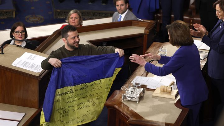 Le président ukrainien, Volodymyr Zelensky, remet un drapeau de son pays signé par des combattants dans la ville de Bakhmout à la présidente de la Chambre des représentants, Nancy Pelosi, le 21 décembre 2022, au Congrès américain, à Washington. (ANNA MONEYMAKER / GETTY IMAGES NORTH AMERICA / AFP)