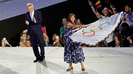 La maire de Paris, Anne Hidalgo, brandit le drapeau olympique à côté du président du Comité international olympique (CIO), au Stade de France, à Saint-Denis (Seine-Saint-Denis), le 11 août 2024. (DIMITAR DILKOFF / AFP)