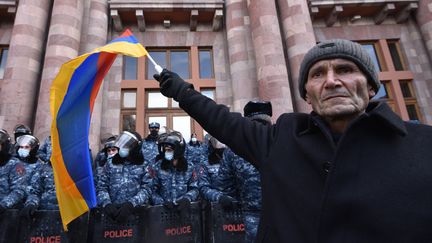 Un homme agite un drapeau arménien devant les forces de l'ordre lors d'un rassemblement pour demander la démission du Premier ministre Nikol Pashinyan, à Erevan le 24 décembre. (KAREN MINASYAN / AFP)