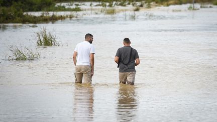 Deux hommes marchent sur une route inondée, dans le Gard, le 14 septembre 2021. (SYLVAIN THOMAS / AFP)