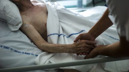 Une infirmière tient la main d'un patient dans le service de soins palliatifs de l'hôpital d'Argenteuil, dans le Val-d'Oise, le 22 juillet 2013. (FRED DUFOUR / AFP)