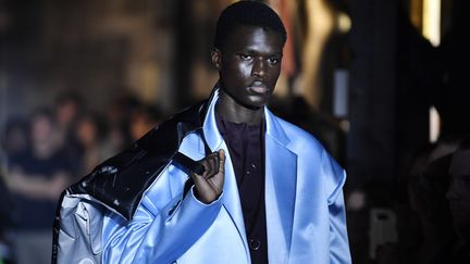 Chez le Belge Raf Simons, c'est une silhouette de dandy punk qui a défilé. Les vestes de costume et les manteaux satinés ont des carrures exagérées, les pulls immenses ont des manches à rallonge et des ouvertures. Les chemises à la mèche rebelle se portent ouvertes sur des hauts formés par des filets à larges mailles qui laissent voir le torse.
 (Julien de Rosa/EPA/Newscom/MaxPPP)