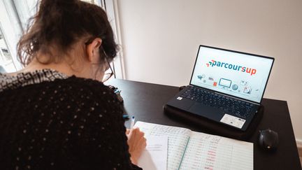 Une professeure travaille à côté d'un ordinateur qui affiche le logo de Parcoursup, à Paris le 26 mai 2021. (LEO PIERRE / HANS LUCAS / AFP)