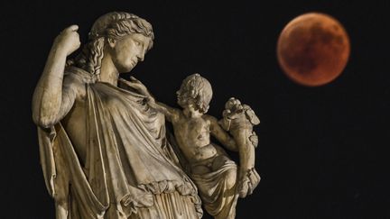 L'éclipse vue depuis la capitale grecque, Athènes, et une statue de la déesse Eiréné. (ARIS MESSINIS / AFP)