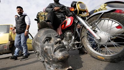 Un combattant des troupes rebelles pose le pied sur la tête découpée d'une statue de l'ancien président syrien Hafez el-Assad à Damas, le 8 décembre 2024.