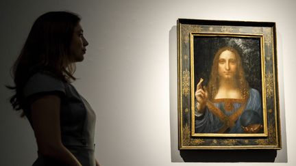 Une employée de Christie's prend la pose devant le tableau de Leonard de Vinci, "Salvator Mundi", le 22 octobre 2017 à New York (Etats-Unis). (TOLGA AKMEN / AFP)