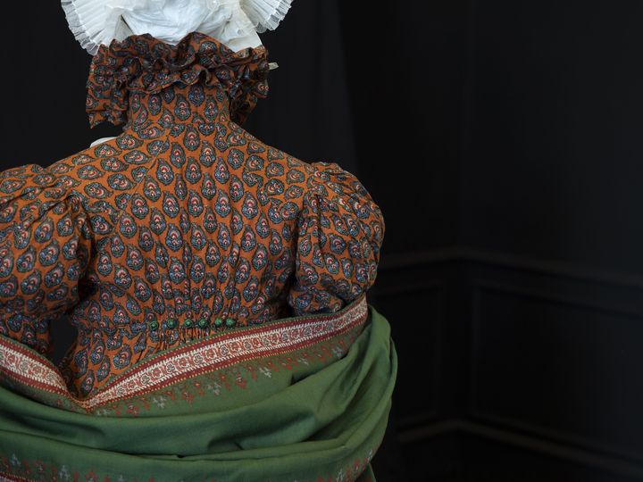 Exposition "Boteh/Beautés Cachemire"&nbsp;au&nbsp;musée provencal du costume et du bijou de Grasse : robe en coton imprimé fond orange à motifs de palmettes, col montant à falbalas et haut de manches ballon. Étole en laine et soie motifs de cachemire. France, vers 1815-1820&nbsp; (Eva Lorenzini)