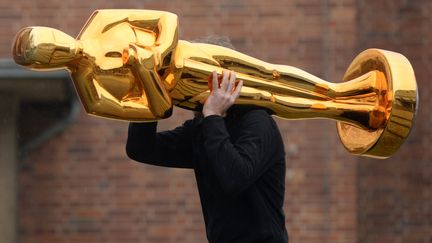 Un homme transporte une statue d'Oscar, à Potsdam (Allemagne), le 23 février 2015. (RALF HIRSCHBERGER / DPA / AFP)